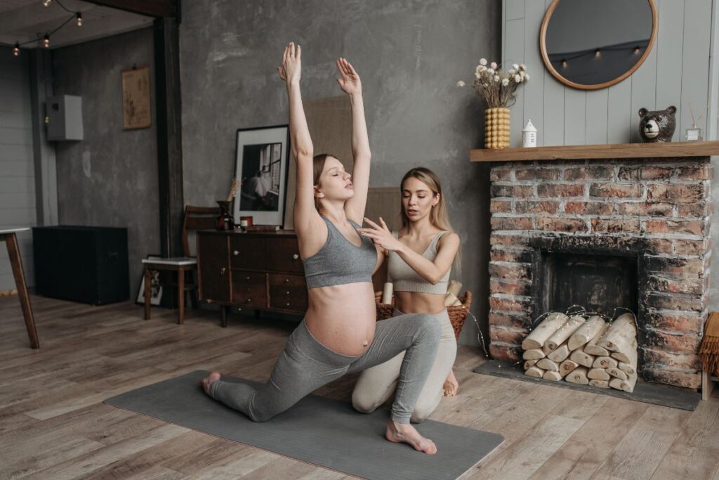 Selecionamos uma imagem simbólica para representar exercícios para grávidas e poder escrever sobre dicas pré, durante e pós gravidez. Na imagem, aparece uma grávida praticando yoga com o auxilio de uma profissional.